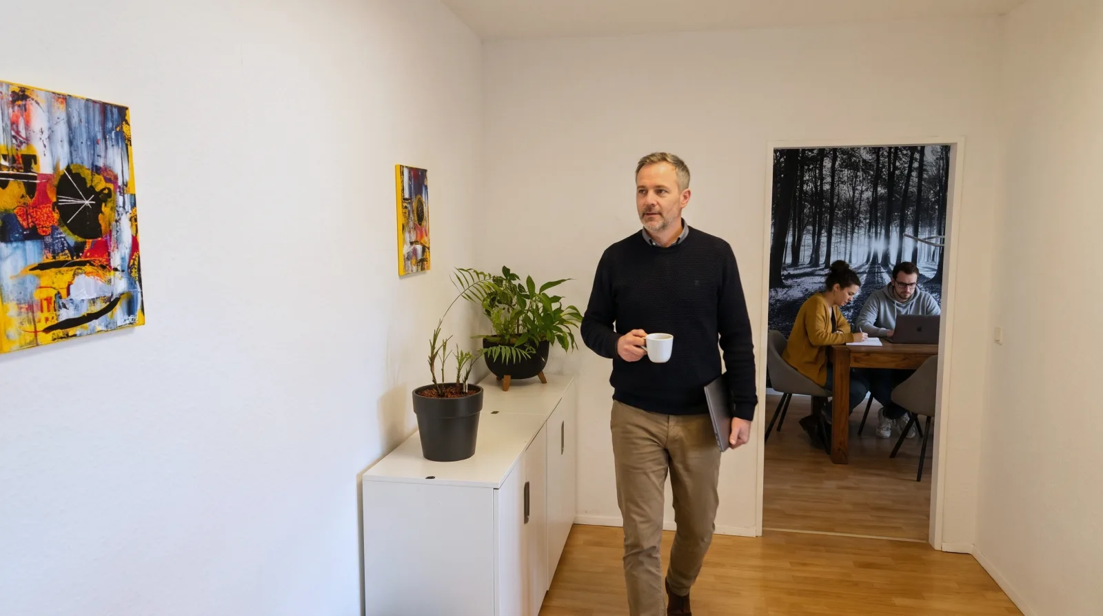 Kollege mit Kaffee und Laptop im Flur des wnm-Büros Leverkusen, im Hintergrund der Besprechungsraum