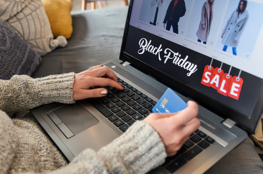 Person kauft online Kleidung mit Kreditkarte, Laptop zeigt SALE-Angebote